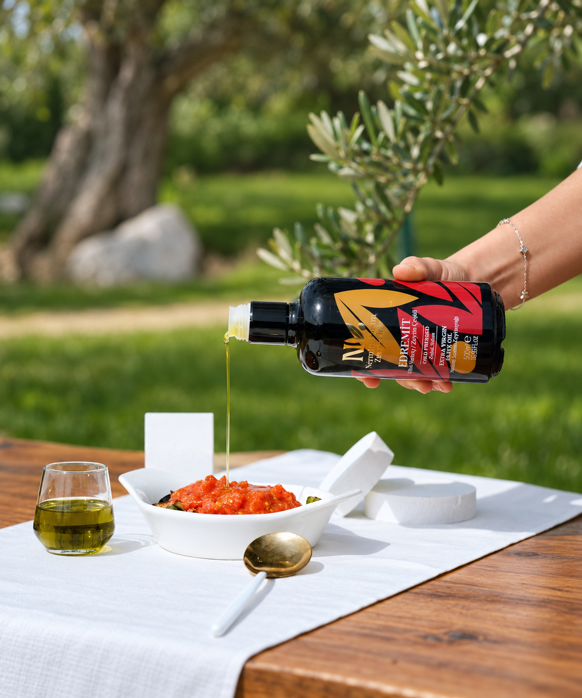 A hand pouring Nermin Everyday olive oil beside a salad outdoors
