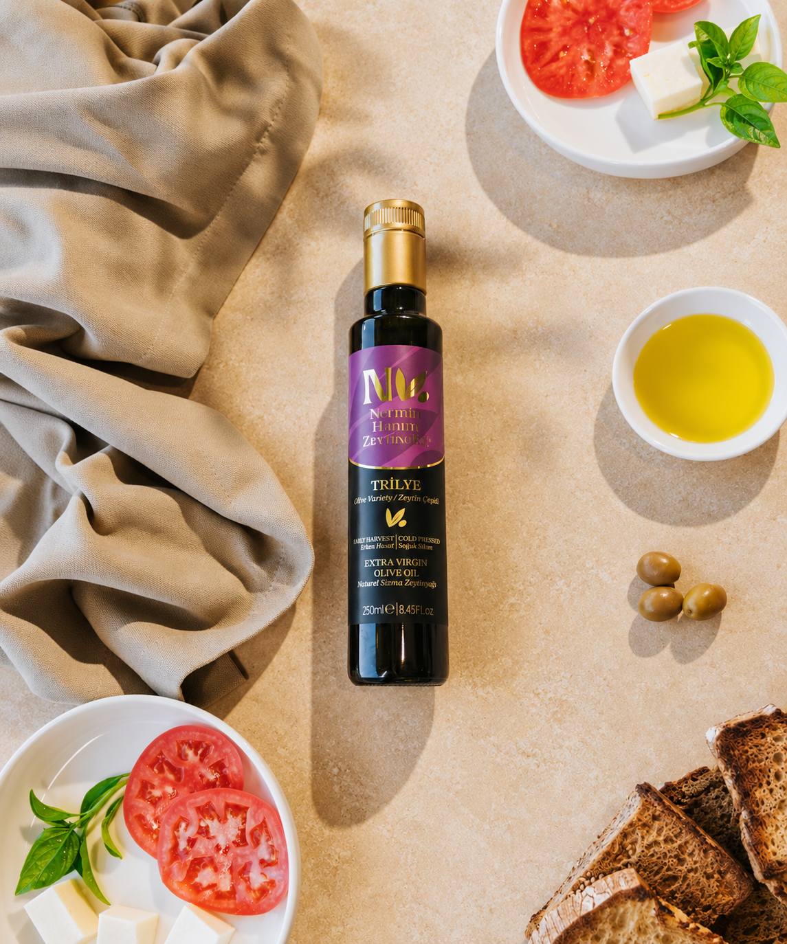 Nermin Trilye olive oil on a table with tomato, bread and a bowl of oil